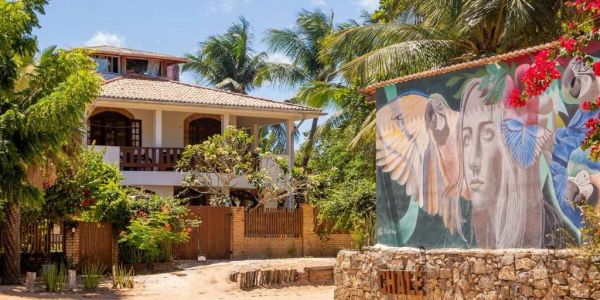 A tropical house with a colorful mural on a stone wall nearby.