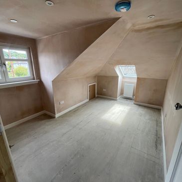 Empty attic room with sloped ceiling and two windows, under renovation.