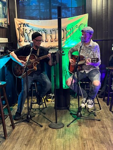 Two musicians playing guitars live on stage.