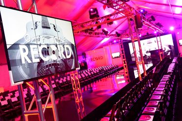 Fashion event runway with 'Off The Record' screens and seating under vibrant pink lighting.