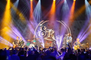 A live band performs on stage with vibrant lighting and a large audience.