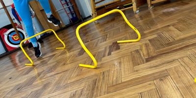 Child jumping over yellow hurdles on a wooden floor indoors.