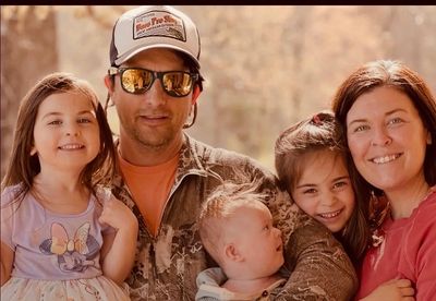 A happy family of five posing outdoors in warm sunlight.