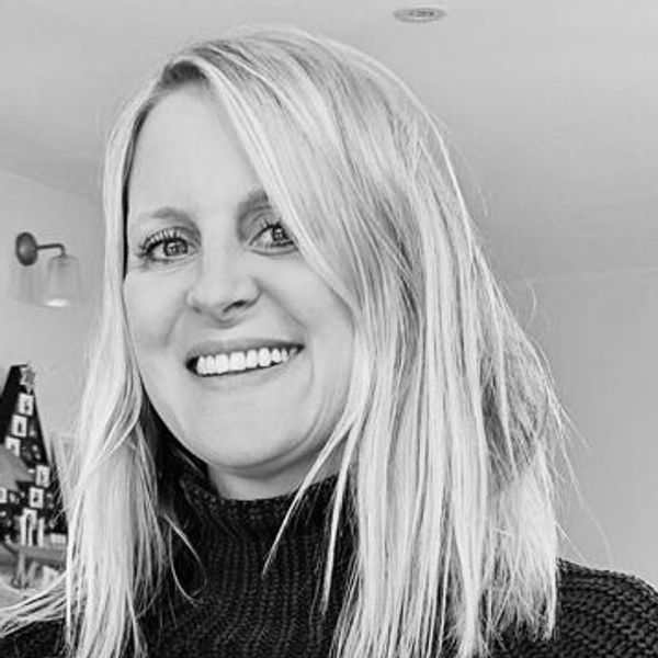 Smiling woman with blonde hair wearing a black sweater indoors.