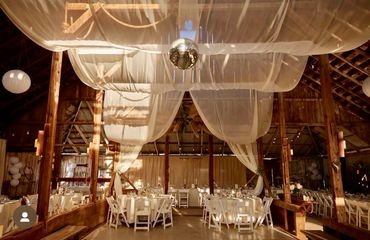 Rustic barn venue decorated with draped fabric and a disco ball for an event.