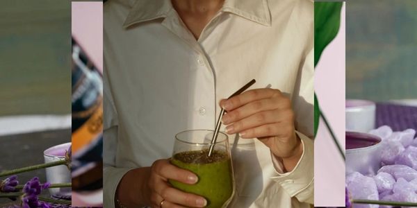 Person stirring a green smoothie in a glass with a metal straw.