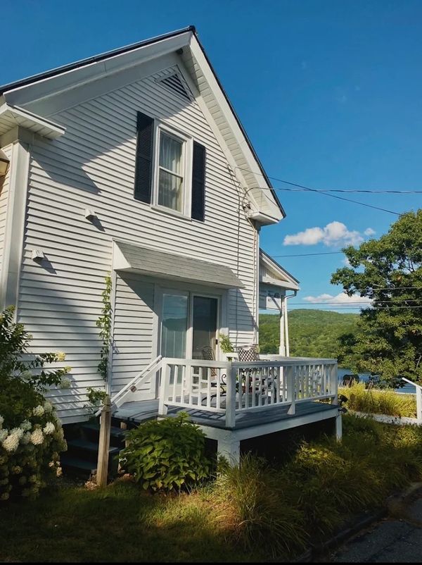 Cozy white house with porch and greenery under a clear blue sky.