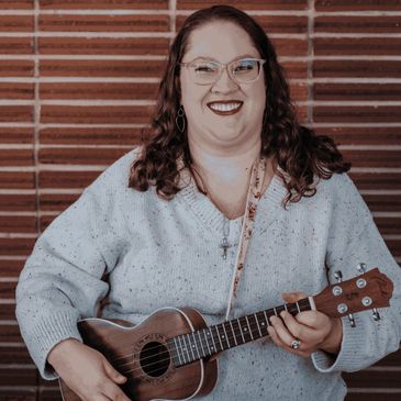 Headshot of Ms. Jenny smiling and holding her brown ukulele at Home Sweet Piano.