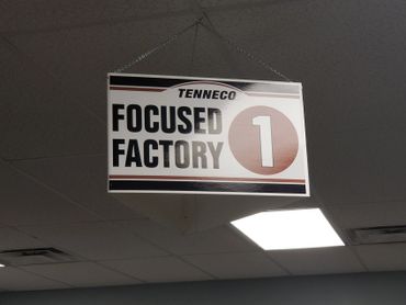 Sign reading 'Tenneco Focused Factory 1' hanging from ceiling.