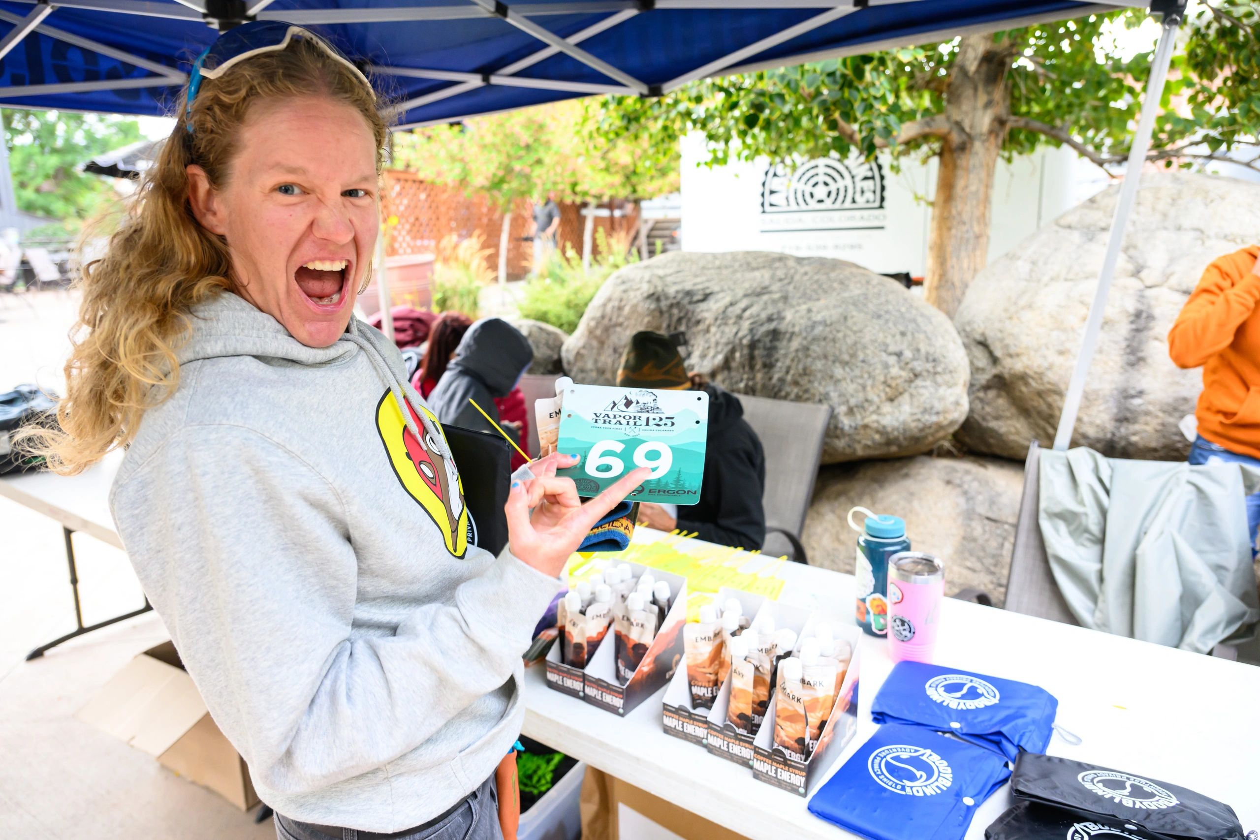 Excited person holding race number 69 at an outdoor event booth.