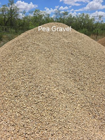 Large mound of pea gravel outdoors under a blue sky.