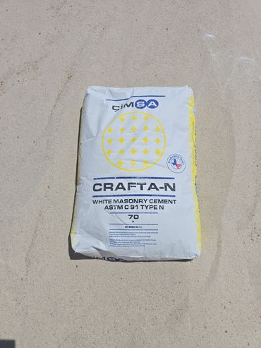 Bag of white masonry cement on sandy ground.