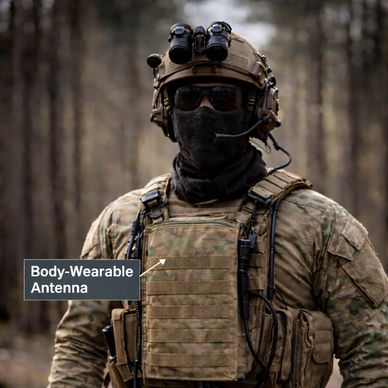 Soldier in tactical gear with body-wearable antenna in forest.