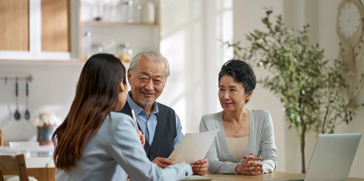 A couple consulting a professional woman across a table with documents and a laptop.