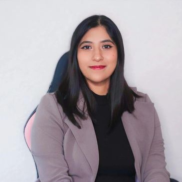 Confident woman with long dark hair in a professional blazer, sitting and smiling.