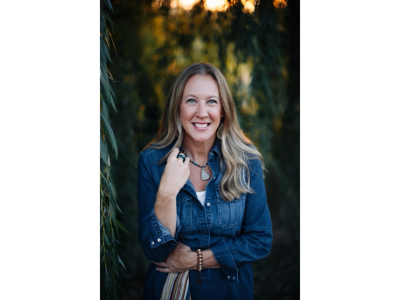 Smiling woman in denim jacket outdoors with warm natural light.