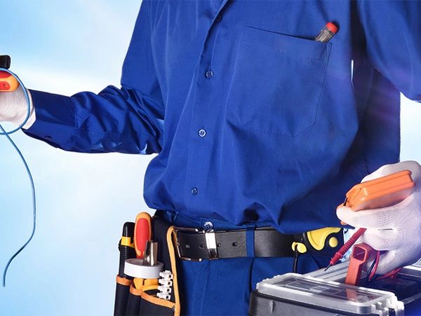 Electrician holding tools and wires, dressed in blue workwear with gloves.
