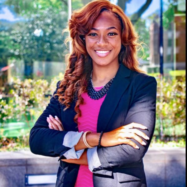 Confident woman in professional attire smiling outdoors with arms crossed.