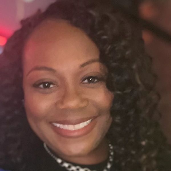 Close-up of a smiling woman with curly hair and a necklace.