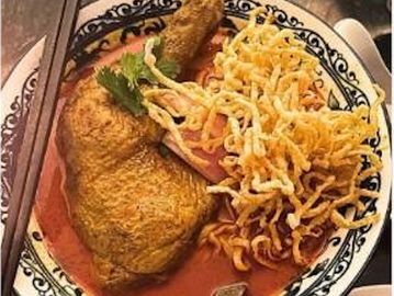 A bowl of crispy chicken curry with fried noodles and garnish.