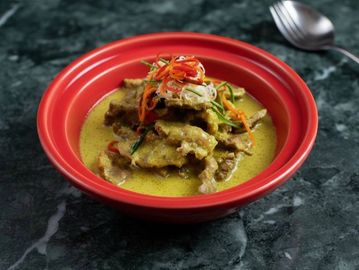 A bowl of savory curry with meat and colorful vegetable garnishes.