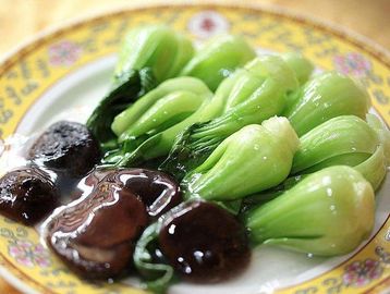 Steamed bok choy with shiitake mushrooms on a decorative plate.