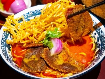 Bowl of spicy noodle soup with crispy noodles and meat slices.