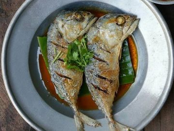 Two grilled fish served with a spicy dipping sauce on a rustic table.