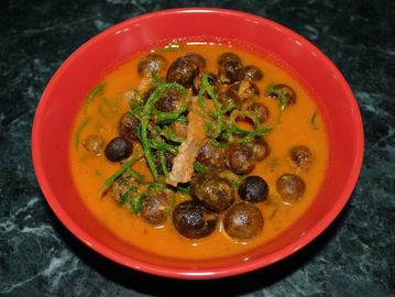 A bowl of mushroom curry with green vegetables in a rich orange sauce.