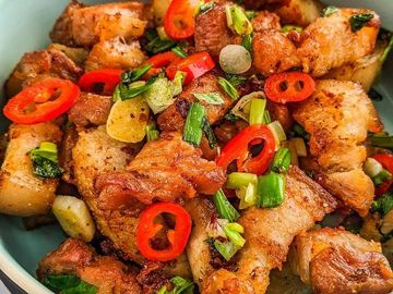 A bowl of crispy fried pork belly garnished with red chili and green onions.
