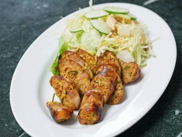 Sliced grilled sausage with fresh cucumber and cabbage salad on a white plate.