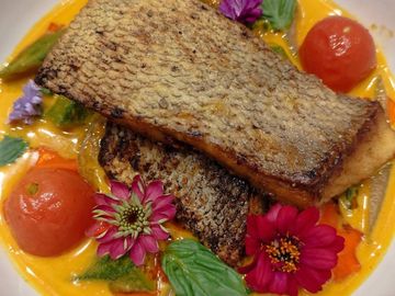 Seared fish fillets on a creamy vegetable curry, garnished with fresh herbs and edible flowers.