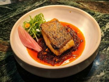 Seared fish fillet on spicy red sauce with garnishes in a white bowl.