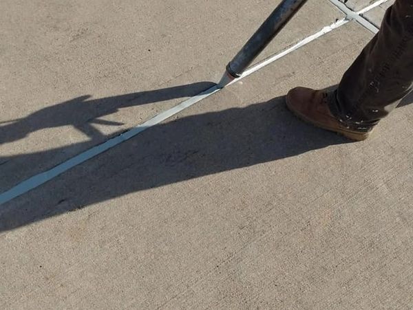 Person sealing cracks on concrete pavement with a tool.