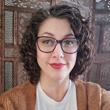 Smiling woman with curly hair, glasses, and a brown cardigan.