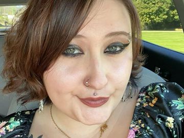 Woman with nose and lip piercings smiling inside a car.