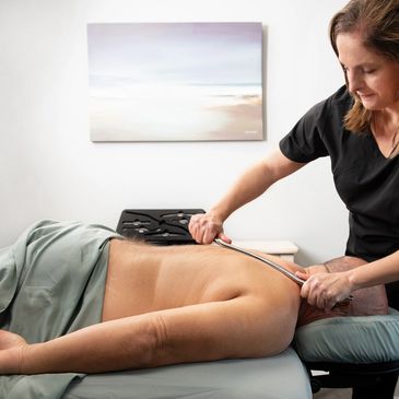 Therapist using a tool to massage a man's back in a calm room.