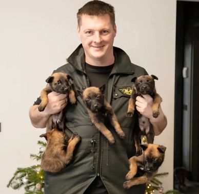 Man holding five adorable puppies, smiling warmly.