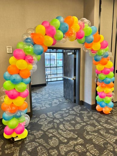 Colorful balloon arch decorates an indoor doorway.