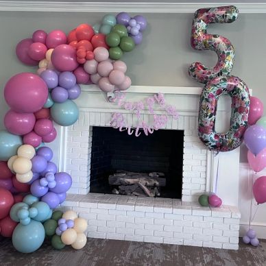 Colorful balloon decorations around a white fireplace for a 50th birthday celebration.