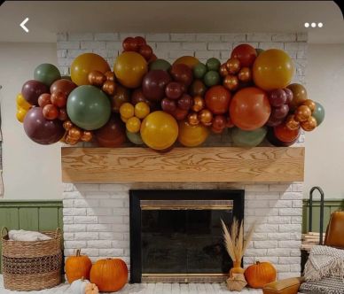 Autumn-themed balloon garland above a fireplace with pumpkins and cozy decor.