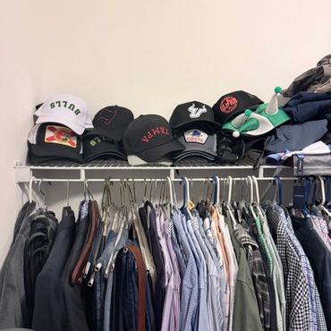 Messy closet shelf with hats and hanging clothes.