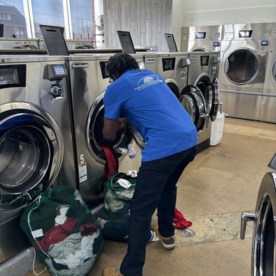 Person loading laundry into a washing machine in a laundromat.