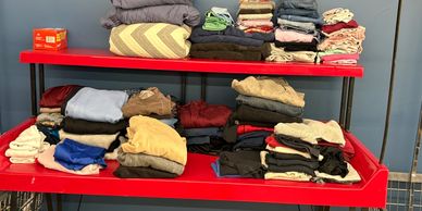 Neatly folded clothes organized on red shelves against a blue wall.