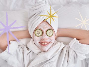 Happy woman with a facial mask and cucumber slices on eyes relaxing in a white bathrobe.