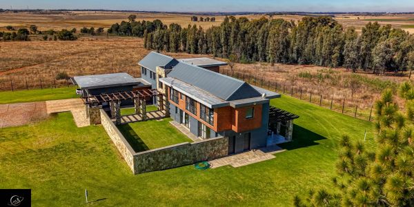 Modern two-story house with stone walls and surrounding lawn in a rural setting.