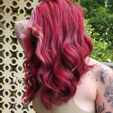 Person with vibrant pink hair, tattoos, and casual outfit outdoors.