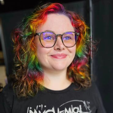 Person with rainbow-colored curly hair and glasses wearing a My Chemical Romance T-shirt.