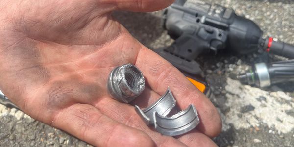 Hand holding damaged metal parts with a power tool in the background.