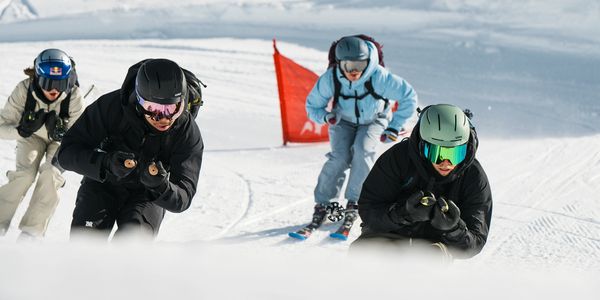 Four skiers racing down a snowy slope in winter gear.
